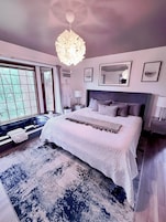 Un dormitorio con una cama grande, una ventana con vistas a árboles, una lámpara colgante y un espejo en la pared.