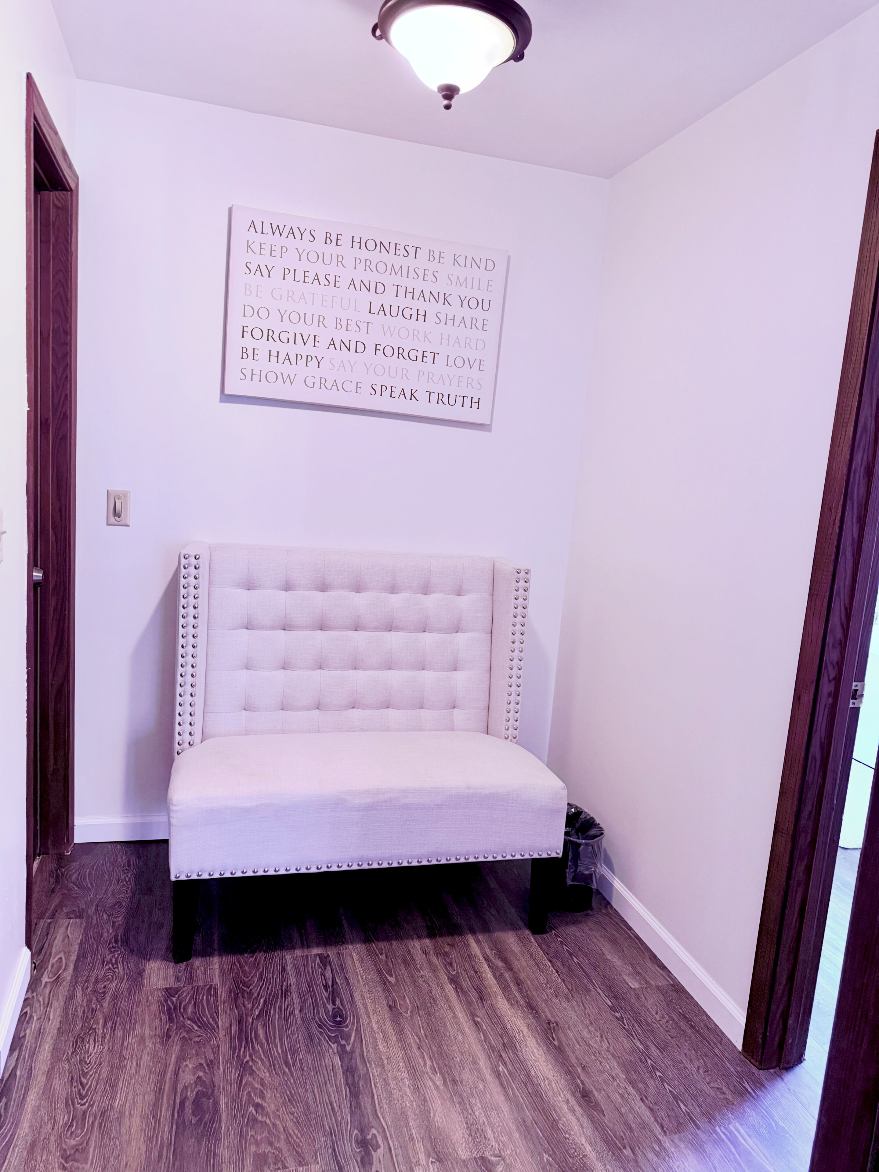 A room with a tufted headboard bed, a motivational quote on the wall, and a wooden floor.