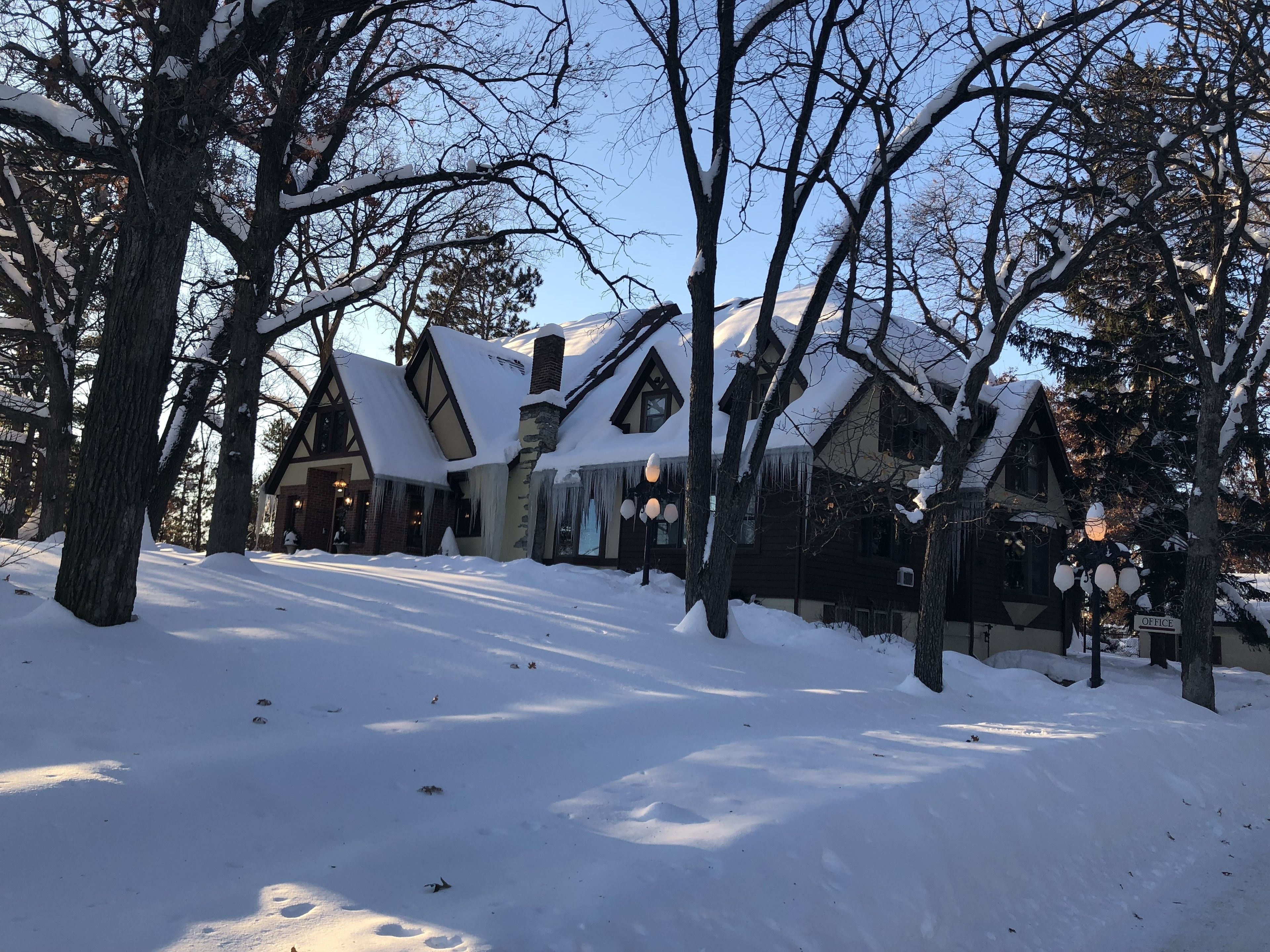 Una cabaña cubierta de nieve con chimenea, estalactitas y un letrero que dice 'OFFICE'.