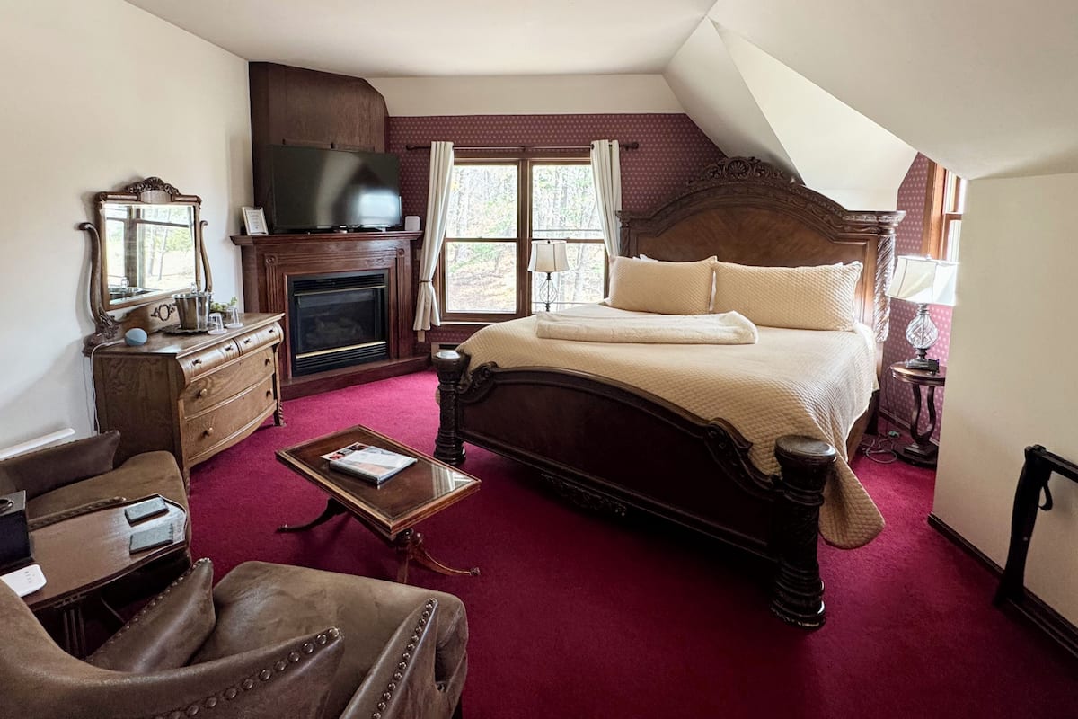 A bedroom with a large bed, a television, a fireplace, and a window with curtains.