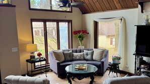 Una sala de estar acogedora con techo de madera, ventanas amplias, un sofá, dos sillones, una mesa de centro y una chimenea.