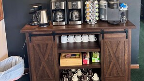 Una estación de café con una pared de pizarra que muestra los mensajes 'Coffee o'clock' y 'but first Coffee', cafeteras y equipo de preparación.