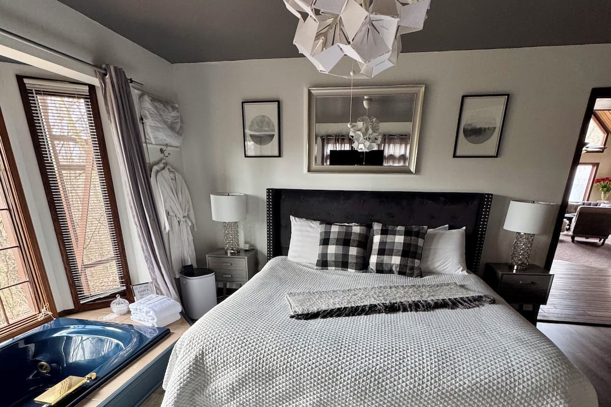 A modern bedroom with a large bed, a bathtub, and a unique ceiling light fixture.