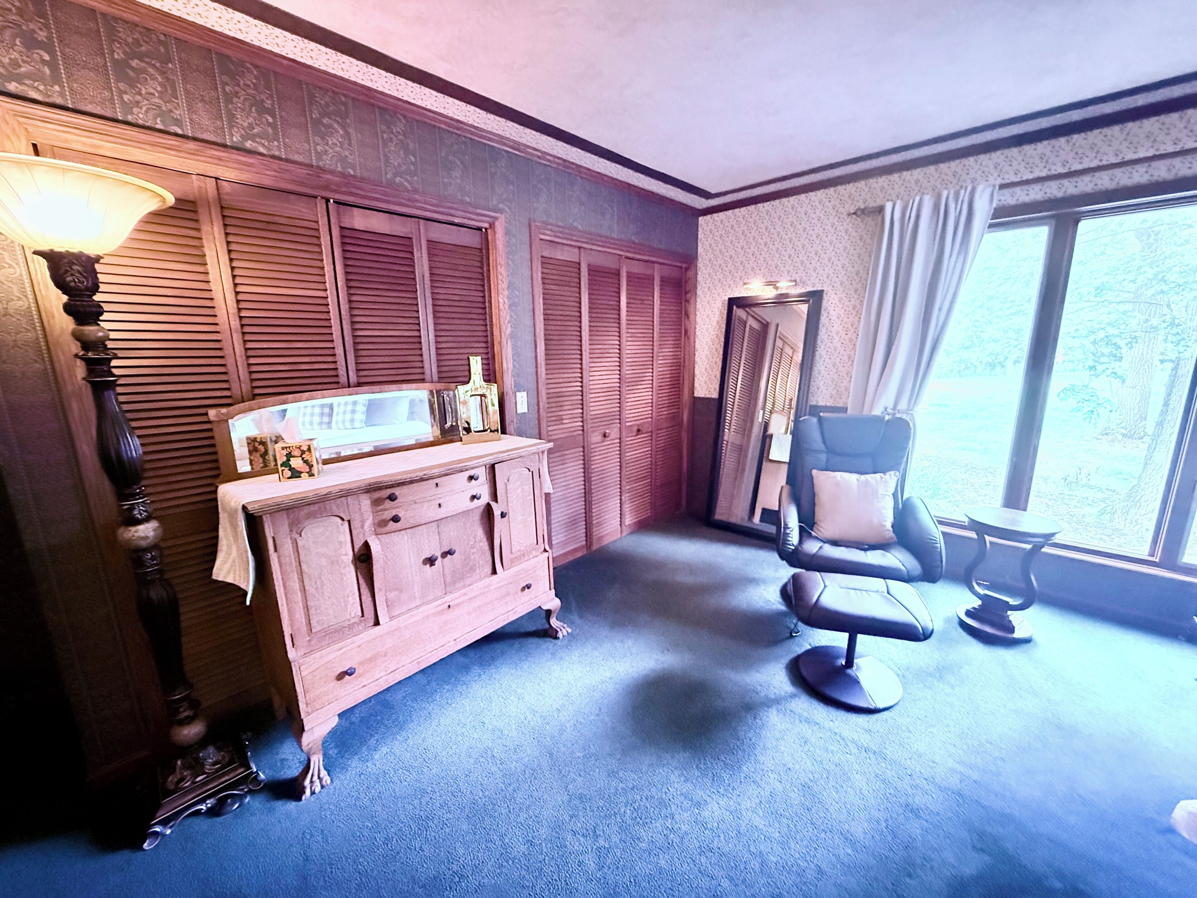 A room with a vanity, a chair, and a large window.