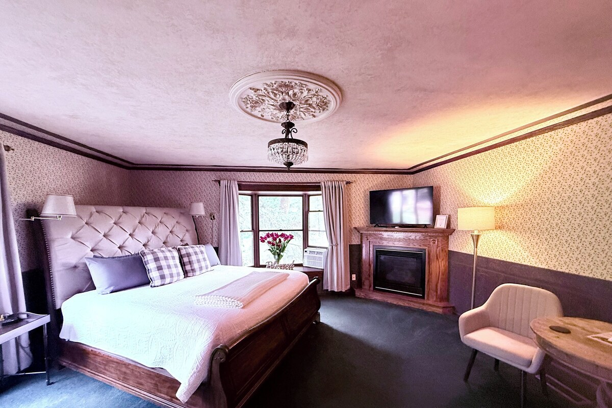 Een hotelkamer met een groot bed, een televisie, een open haard, een stoel en een raam met gordijnen.