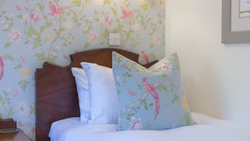 Un dormitorio con papel tapiz floral, cabecera de madera y almohadones decorativos.