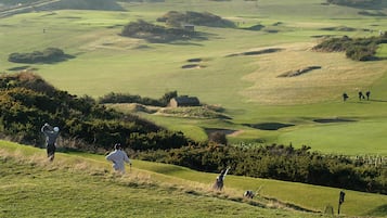 A golf course with rolling hills, bunkers, and a distant water hazard.