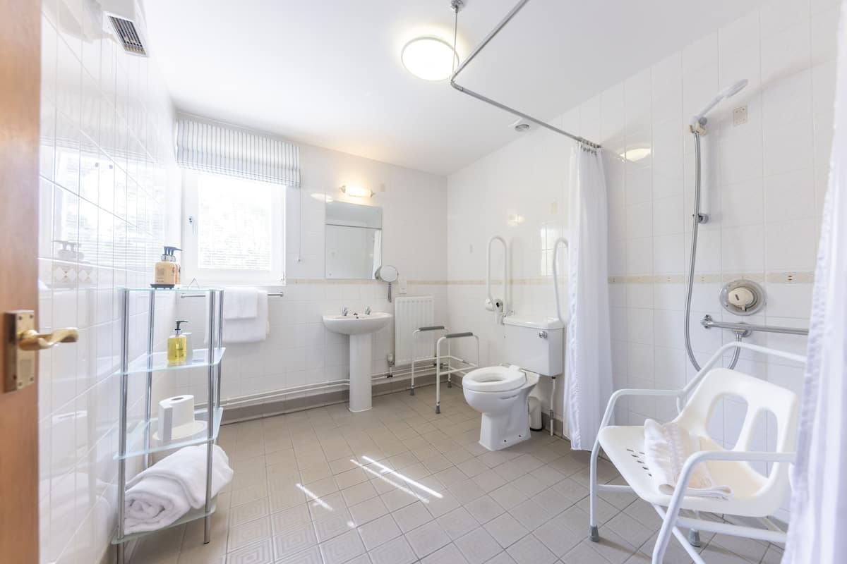 A bathroom with a toilet, sink, shower, and a glass shelf with toiletries.