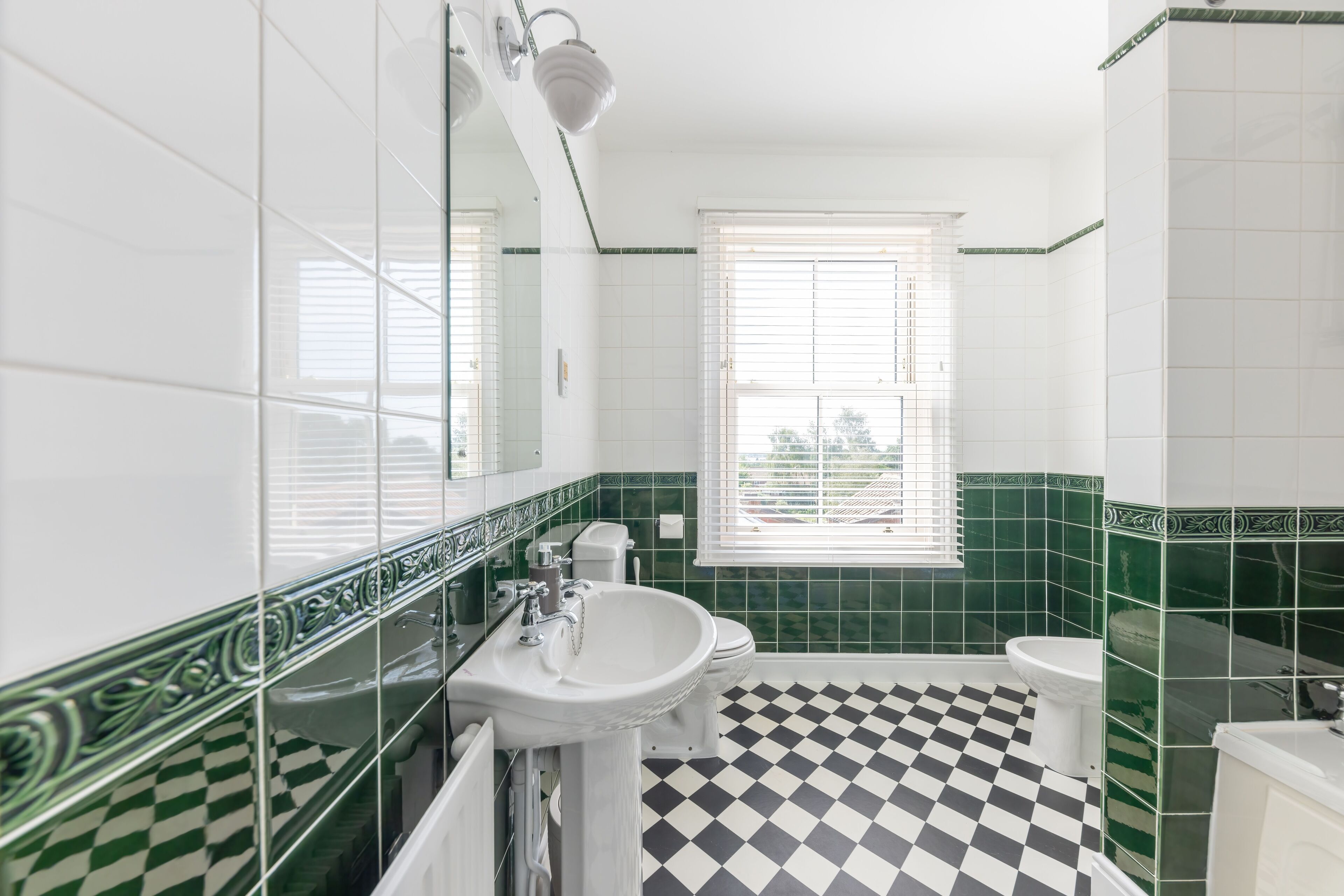 Een badkamer met een zwart-wit betegelde vloer, een wastafel, een toilet en een raam met jaloezieën.