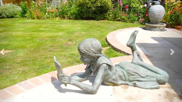 Un jardín con una estatua de un niño leyendo.