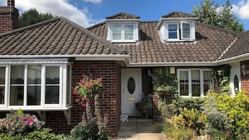 A two-story house with a tiled roof, a brick facade, and a front garden with various plants and flowers.