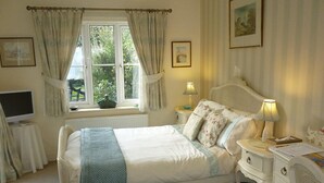 Un dormitorio con cama, mesitas de noche, una lámpara, una ventana con cortinas y un televisor sobre un mueble.