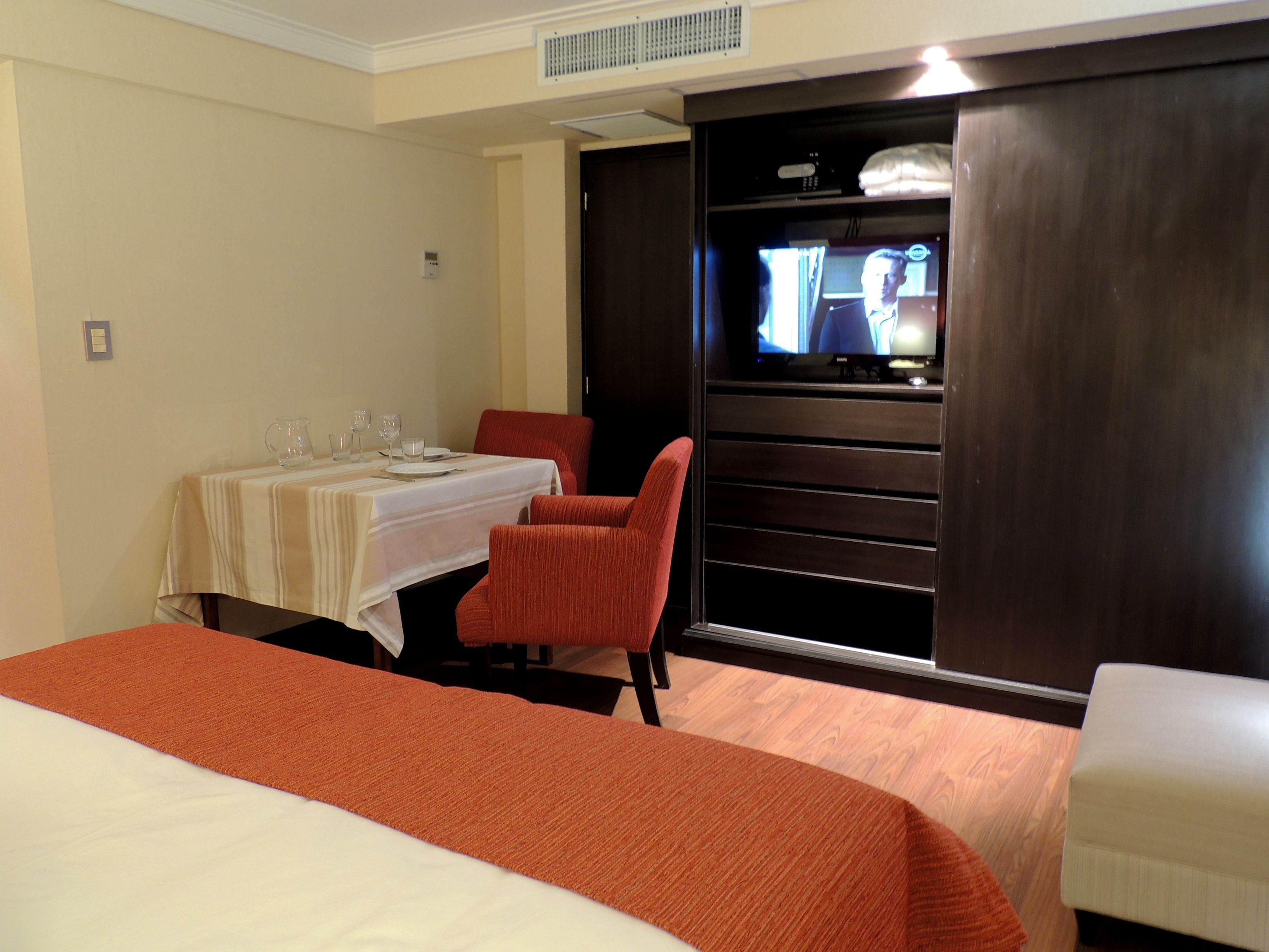 A hotel room with a bed, a dining table set with glasses and plates, a TV, and a red chair.