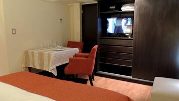 A hotel room with a bed, a dining table set with glasses and plates, a TV, and a red chair.