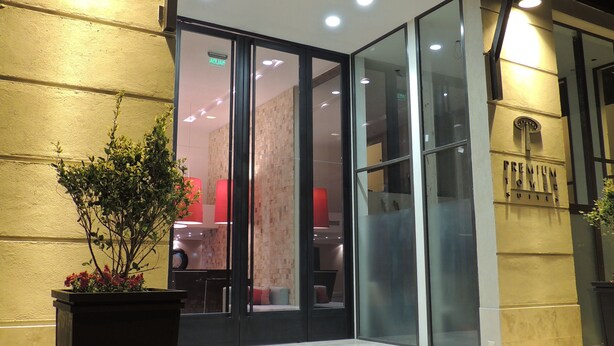Entrada de hotel con puerta de cristal, escalones que la conducen y una planta en maceta al frente.