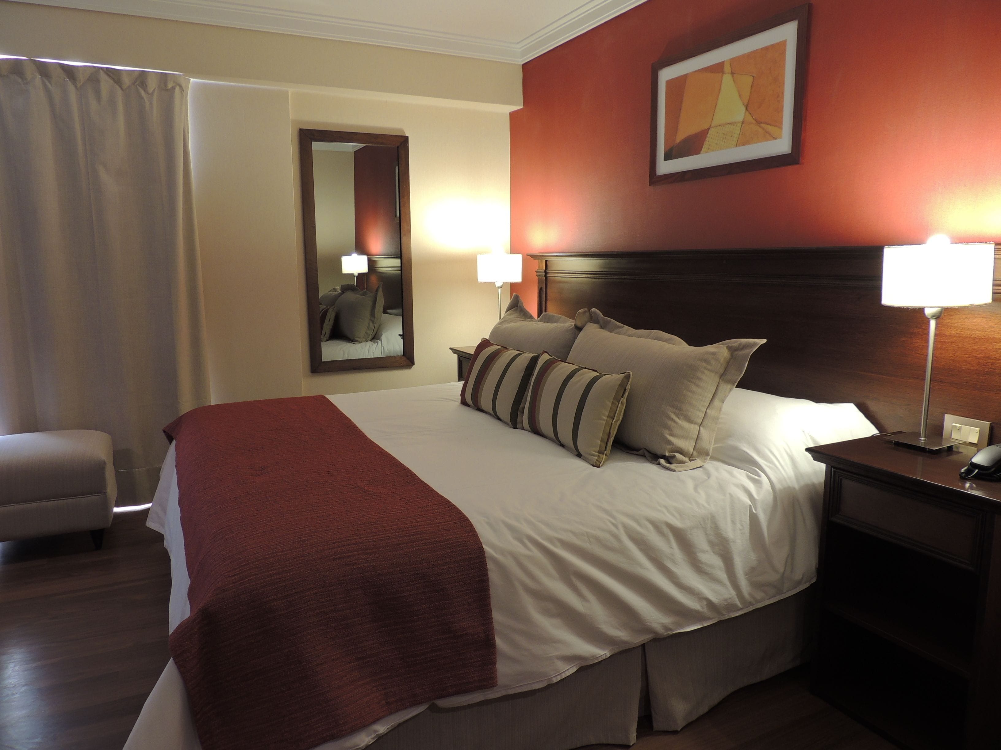 A hotel room with a large bed, two bedside lamps, a nightstand, a chair, and a mirror on the wall.