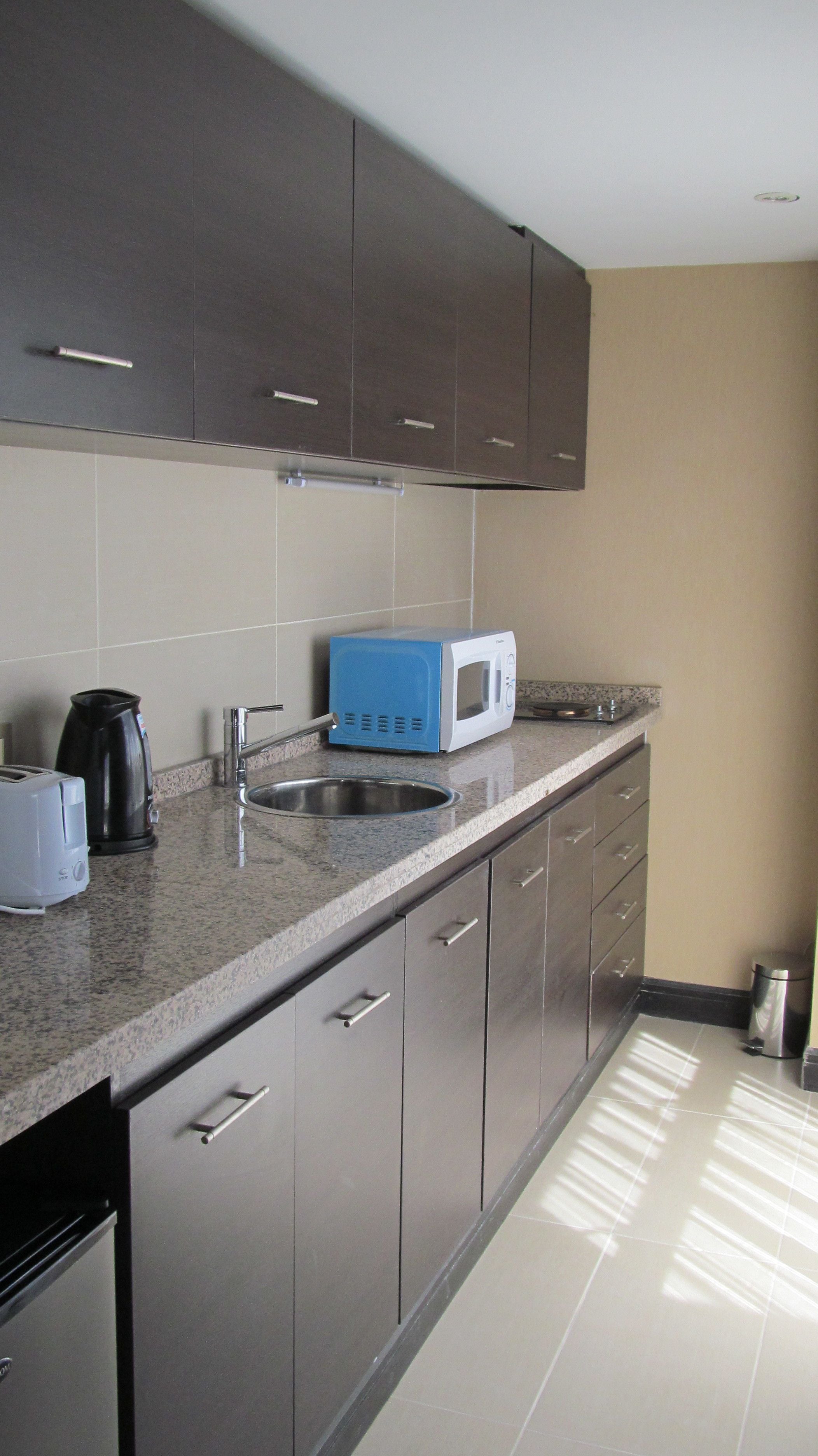 Una cocina moderna con armarios grises, un lavamanos de acero inoxidable, un microondas azul y una tetera.