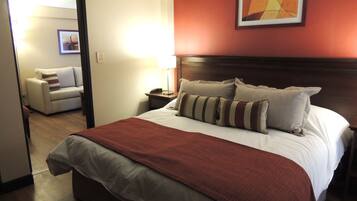 Una camera d'albergo con un letto grande, un comodino, una lampada, una sedia e un quadro appeso al muro.