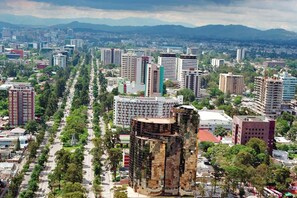 A cityscape with a prominent building featuring a unique facade and a large, modern structure with a patterned exterior. - Laguna Sky (Guatemala City)