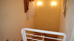 Un escalier étroit avec une main courante blanche, des murs de couleur beige et un luminaire.