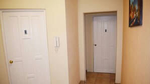 Un couloir avec deux portes blanches, l’une portant la lettre « B » et un interrupteur sur le mur.