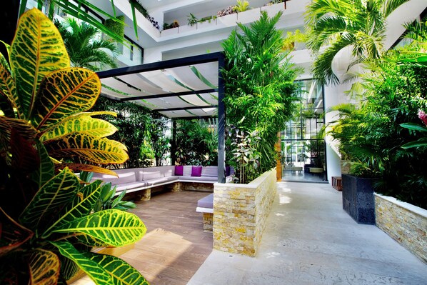 A modern indoor atrium with a central seating area, surrounded by lush greenery and stone walls.