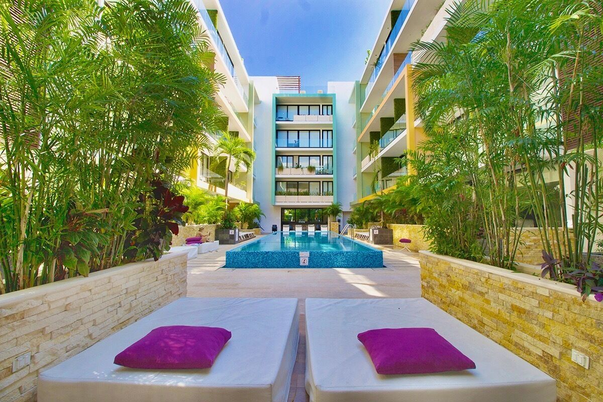 A pool area with two lounge chairs, surrounded by greenery and a building with multiple balconies.