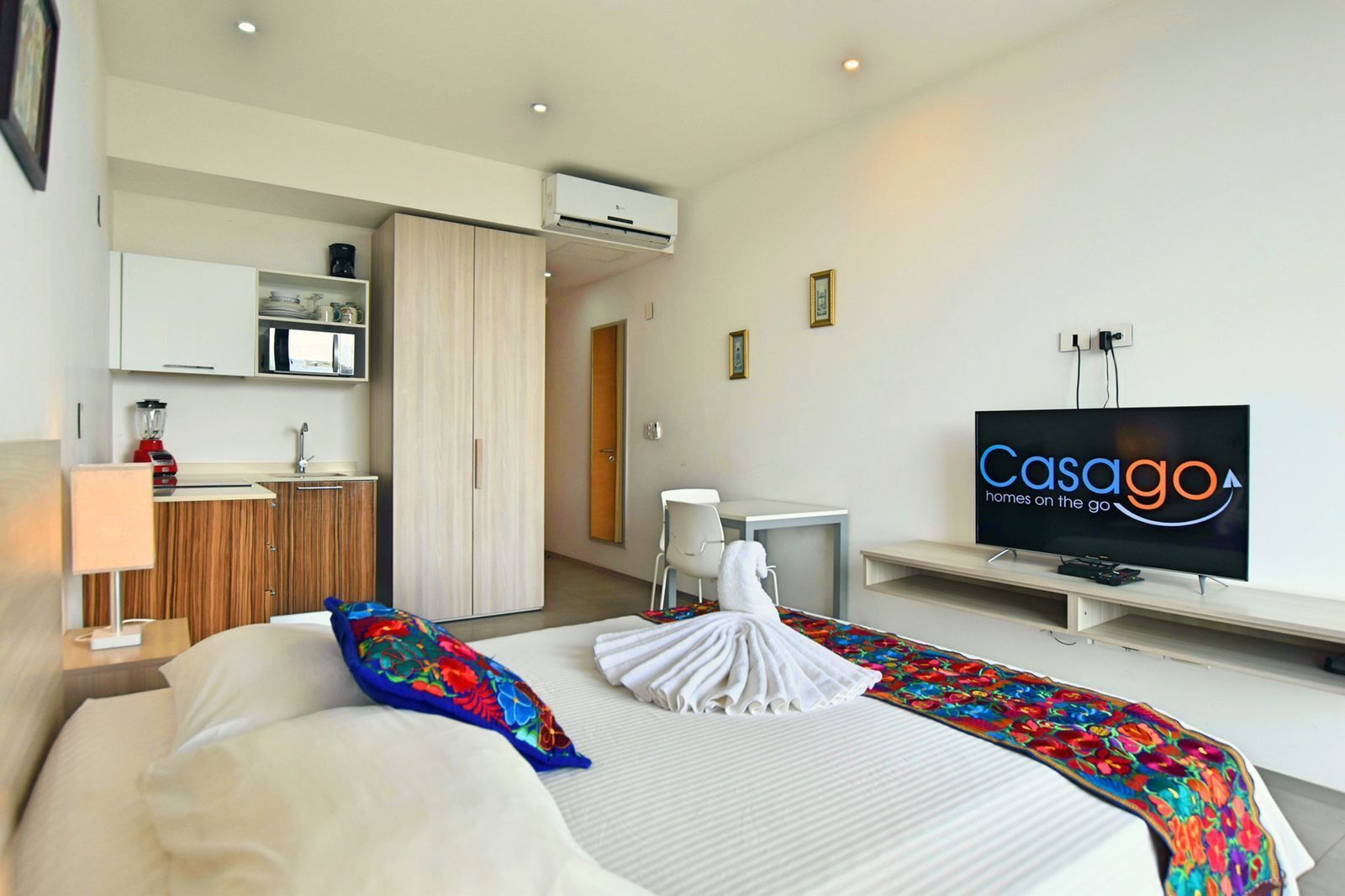 A hotel room with a bed, a desk, a television, and a kitchenette.