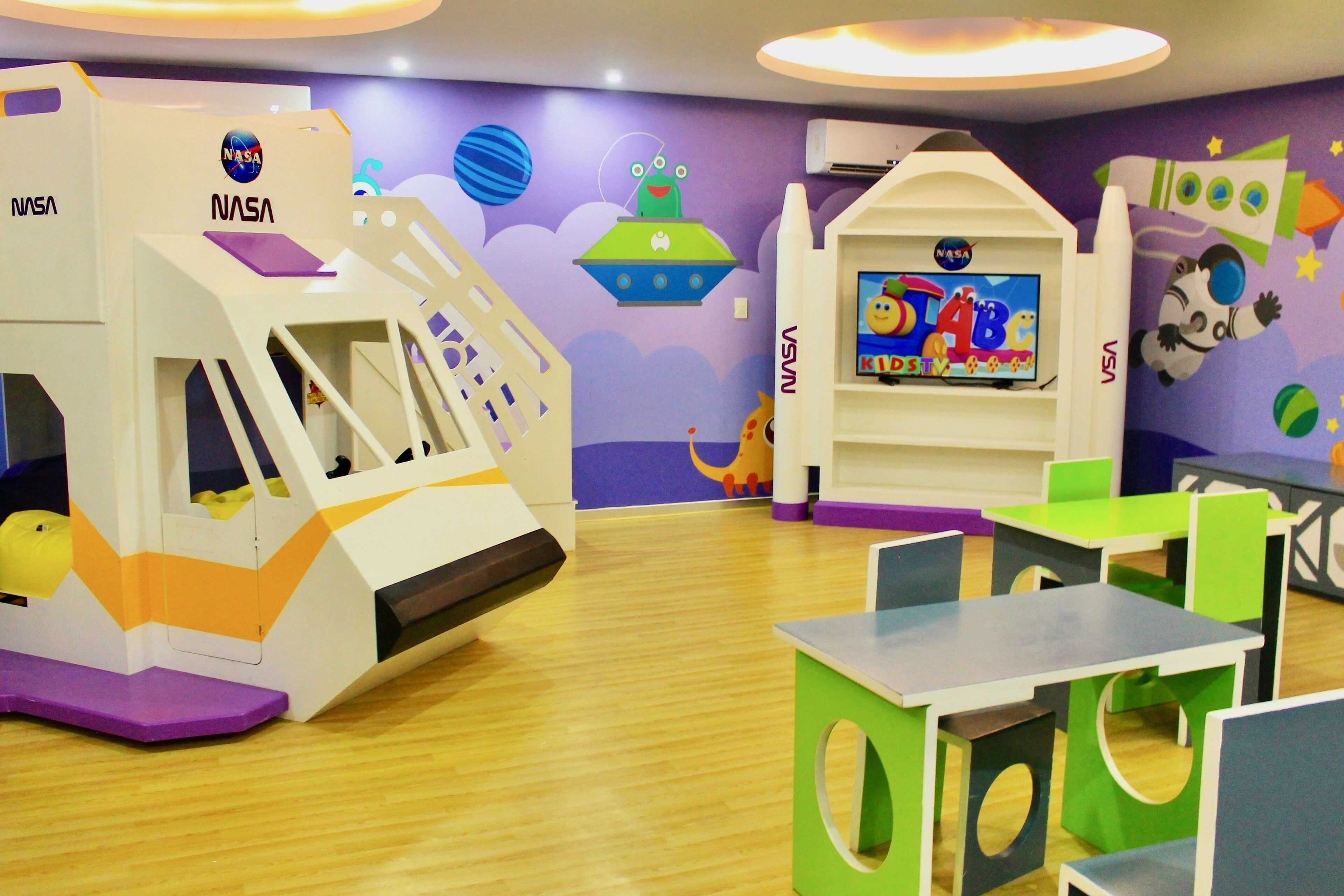 A children's play area with NASA-themed play structures and a TV screen displaying educational content.