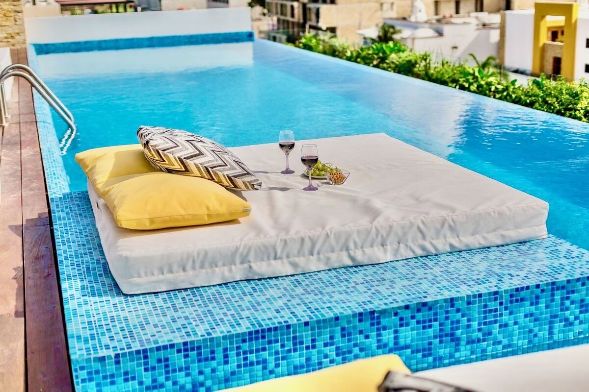 Un espace aménagé au bord de la piscine, avec un fauteuil de relaxation, des coussins et un plateau contenant des verres et des raisins.