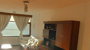 Um quarto com piso de madeira, um sofá, um armário e um lustre.