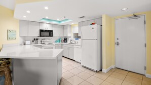 A modern kitchen with white cabinetry, a central island, a microwave, a refrigerator, and a sink. - 🌅 Prime View Condo — Gulf Strand Resort, St. Pete Beach (St Pete Beach)