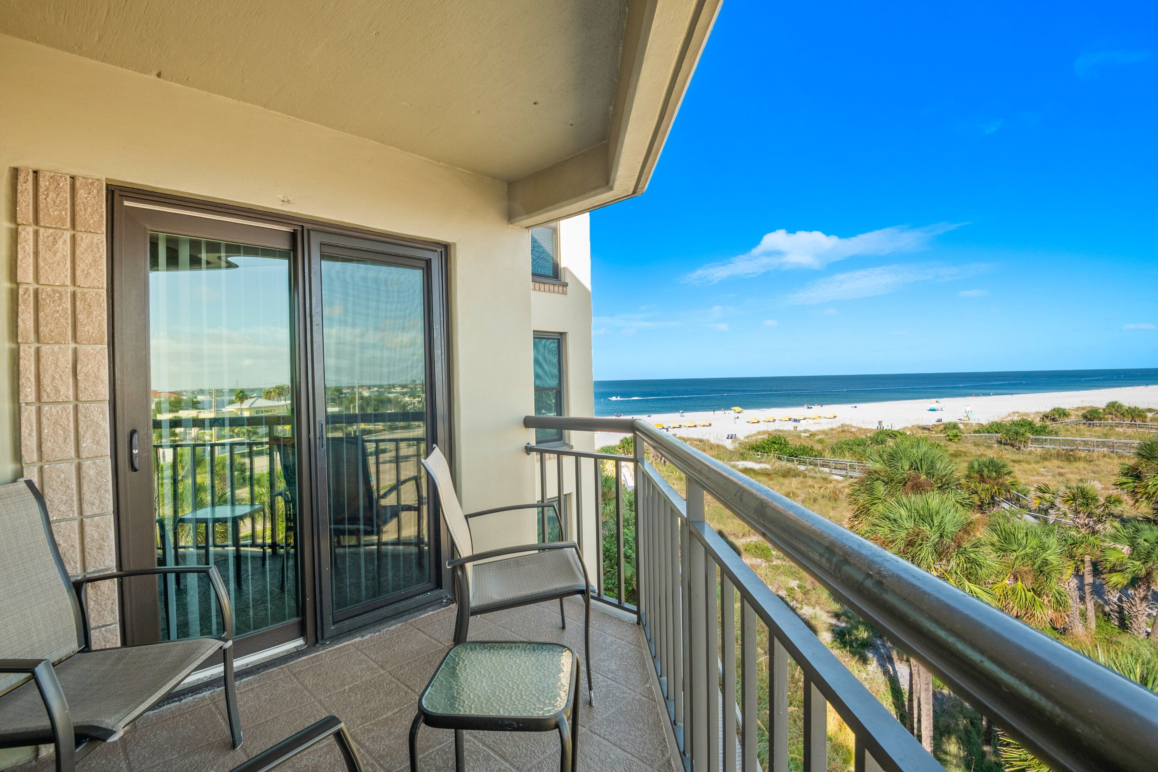 A balcony with two chairs and a glass door leading to a patio area.
