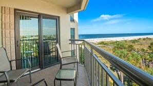 A balcony with two chairs and a glass door leading to a patio area. - 🌅 Prime View Condo — Gulf Strand Resort, St. Pete Beach (St Pete Beach)