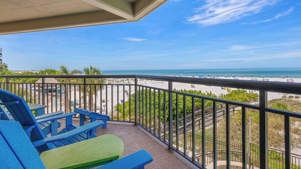 A balcony with blue and green chairs, a view of the beach, and a clear sky.