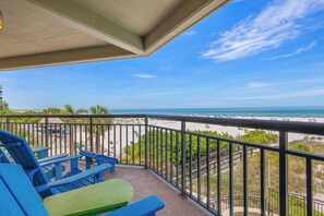 Een balkon met blauwe en groene stoelen, uitzicht op het strand en een heldere lucht.