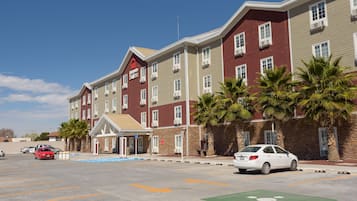 Een hotel met meerdere verdiepingen, met een gevel in rood en beige, een overdekte ingang en palmbomen ervoor.