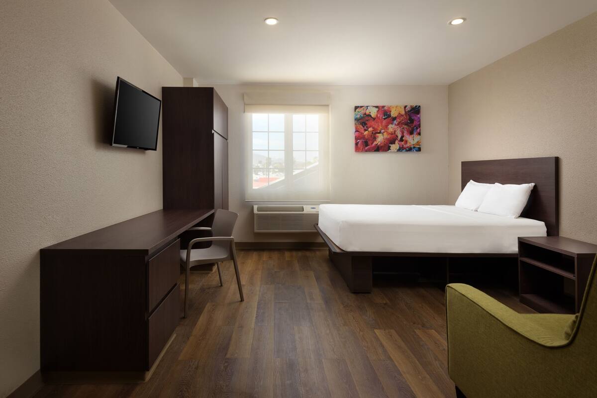 A hotel room with a bed, desk, chair, TV, and a window with a city view.