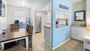 Cocina compacta con comedor, refrigerador y un letrero que dice “Gather Here”.