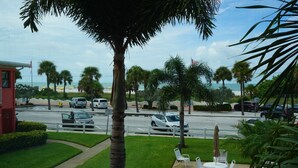 Vista de una calle con coches aparcados, palmeras y una playa al fondo.