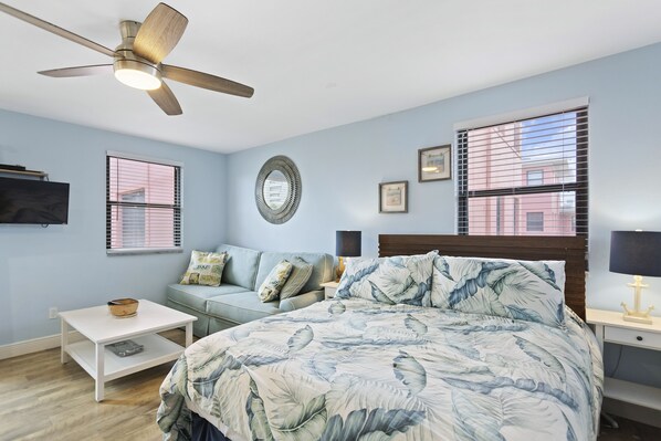 A bedroom with a bed, a ceiling fan, a sofa, a coffee table, and a TV on the wall.