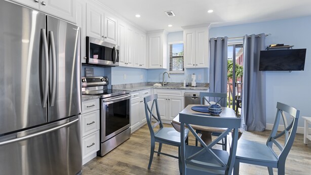 A modern kitchen with stainless steel appliances, white cabinets, and a dining area with blue chairs.