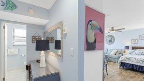 A bedroom with a bed, a desk, and a chair. There is a mirror on the wall and a window with blinds.