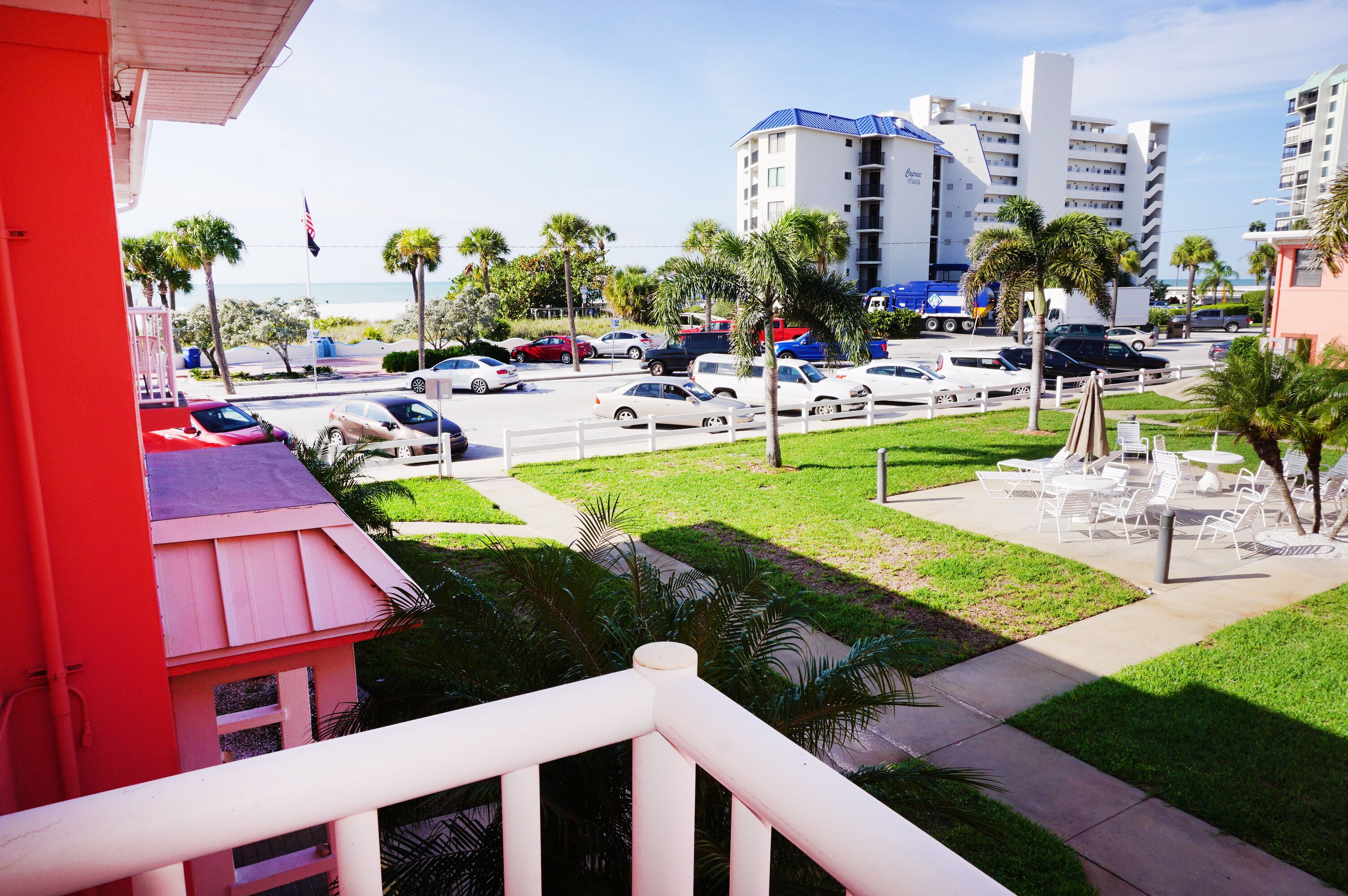 Un hotel de fachada roja, un estacionamiento con varios autos y vista a la playa y al océano.