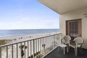 A balcony with a view of the beach, two chairs, and a door. - Sea Breeze 402 | Gulf-Front Comfort with Balcony Sunsets & Walkable Adventure (Madeira Beach)