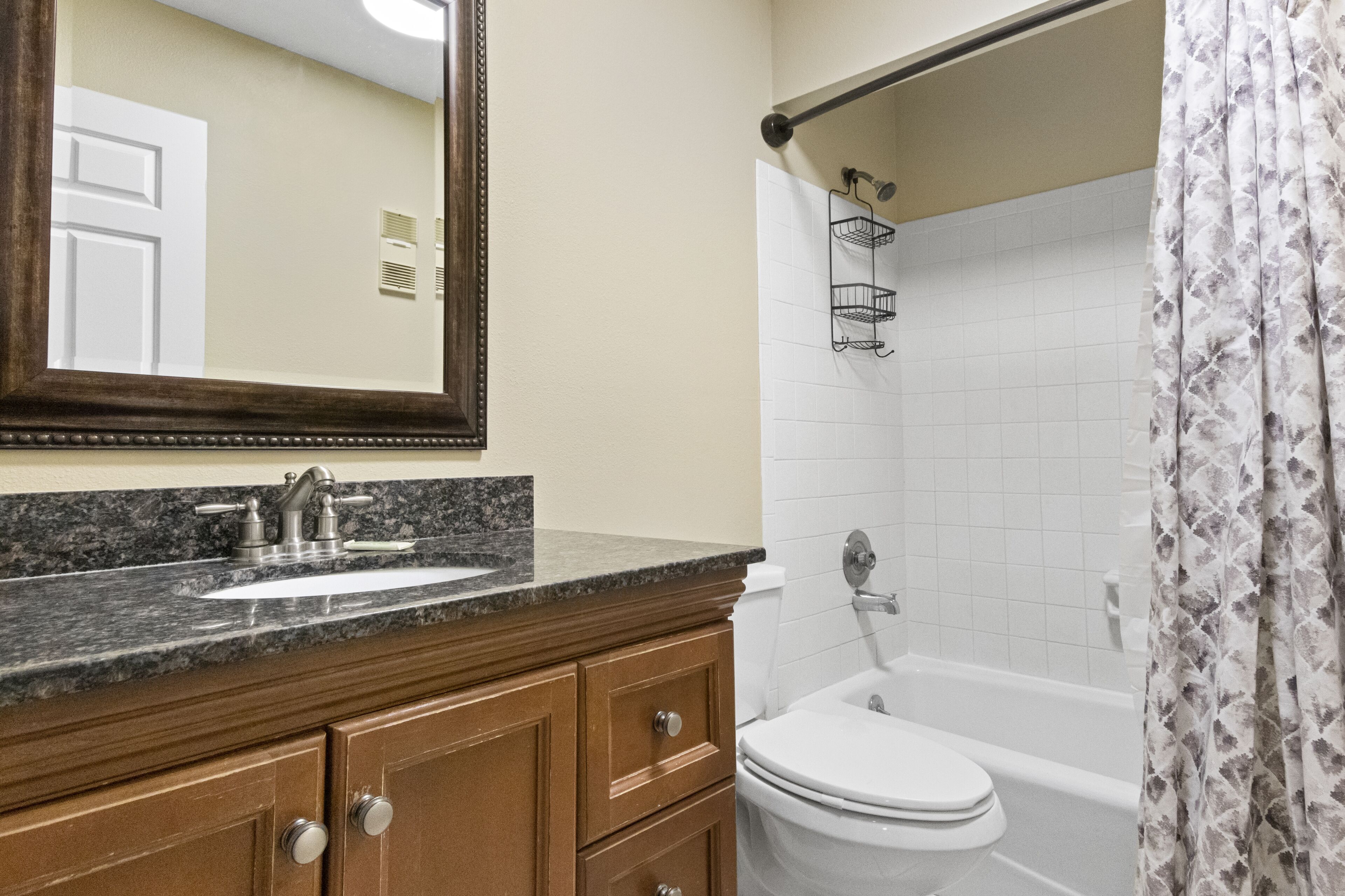 A bathroom with a sink, mirror, wooden vanity, toilet, and bathtub.