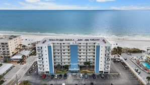 Un hotel de varios pisos con un detalle azul en la torre central, situado cerca de una playa y con un estacionamiento frente a él.