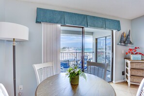 Enjoy a beach view from the large window, with a dining table, chair, and lamp.