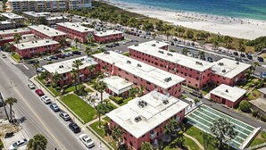 A coastal residential area with multiple red-roofed buildings, a beach, and a clear blue sky.
