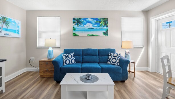A living room with a blue sofa, a white coffee table, and a painting of a beach scene.